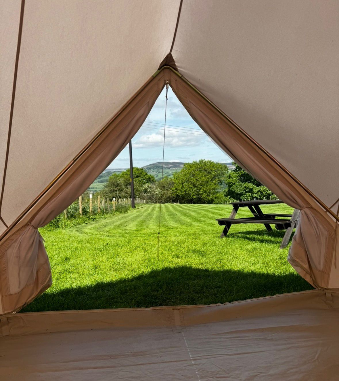 View across Wharfedale from the family glamping teepee doorway at Ghyll House Campsite, with a picnic bench on the campsite field