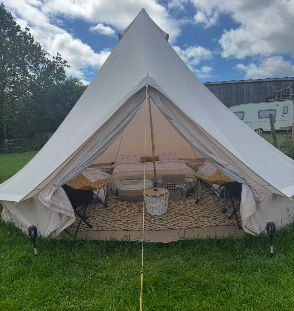The family glamping bell tent at Ghyll House Campsite with a double bed and wicker chairs, set on the campsite field