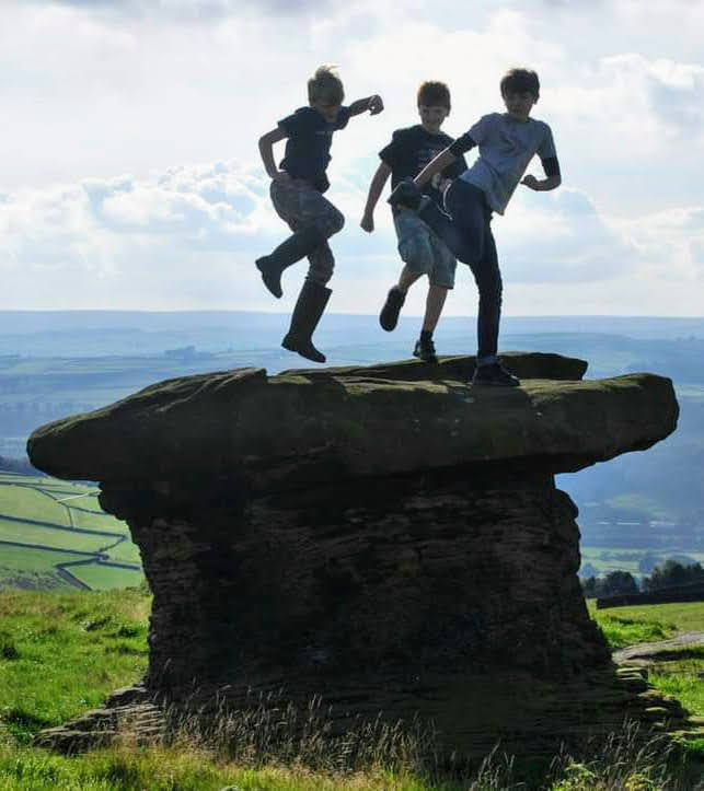 Children leaping from the mushroom-shaped Doubler Stones with the Aire Valley behind