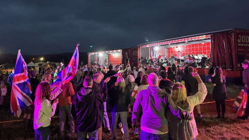 Crowd waving Union Jack flags in front of the stage at Proms on the Farm, Silsden, at dusk